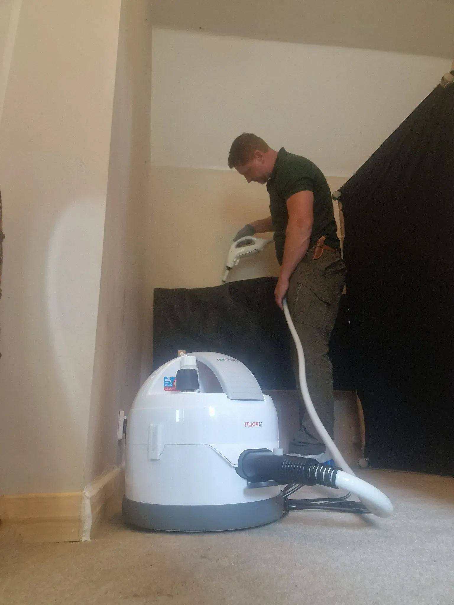 A Tech Country Pest Control technician using a steam cleaner on a wall or furniture as part of an eco-friendly bed bug treatment.